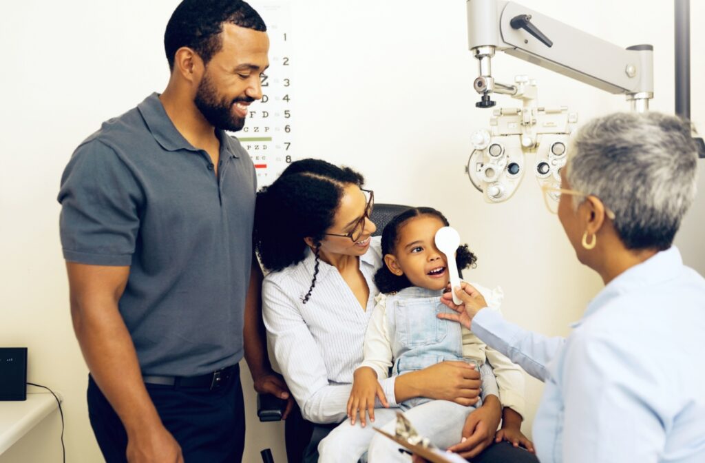 A child held by their parents has their eye covered by an optometrist during a vision test.