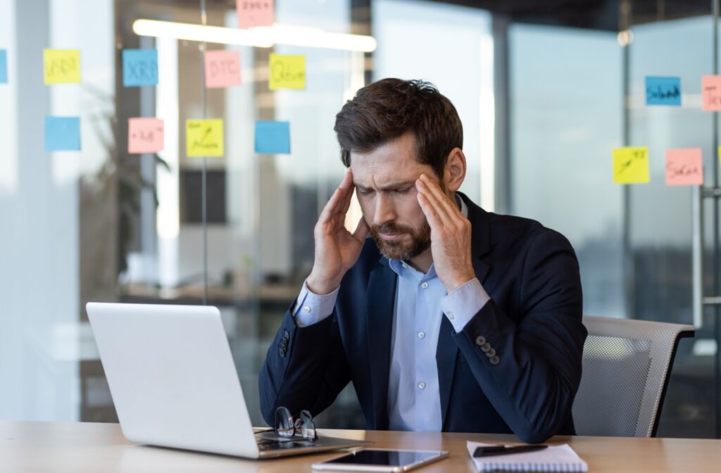 A person soothes their temples to ease a headache while working on a laptop.