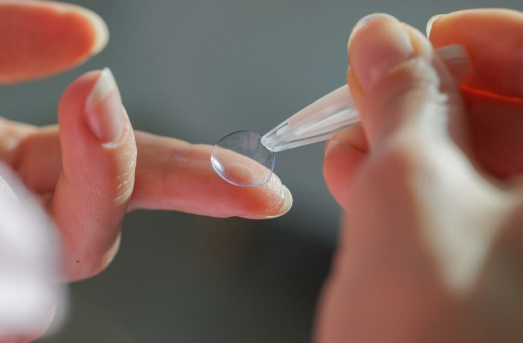 A close up of someone using contact lens tweezers to pick up a contact lens off their finger